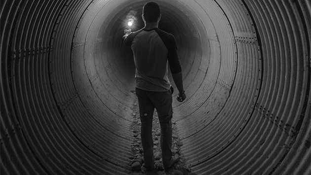 Man standing in dark tunnel and holding a lantern